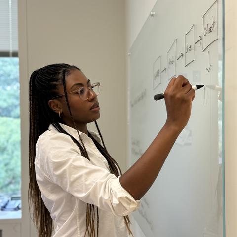 Ashley Hartwell, a researcher, stands in her office and writes concepts down on a glass board. 