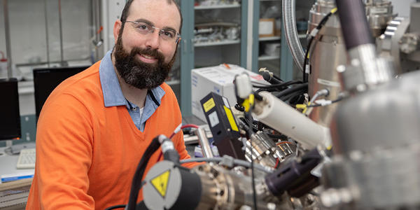 Trey Diulus poses sitting in the lab with a large, complex scientific instrument in the foreground.