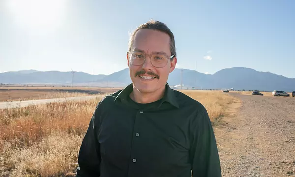 Zach Grey poses outdoors with wind turbines in the background. 