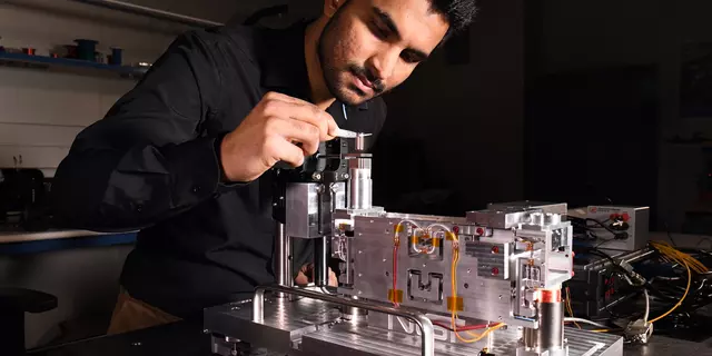 A person in a black shirt works on a mechanical device in a lab setting.