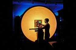 Man with a video display stands in front of a big orange orb of light