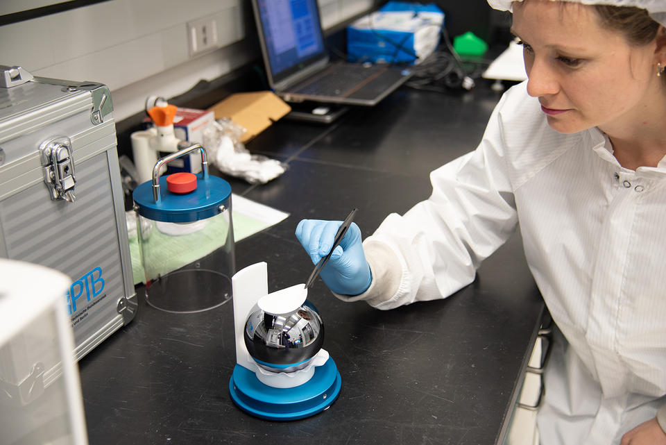 A researcher uses tweezers to adjust a white pad resting on a silvery sphere sitting in a special holder on a lab table. 