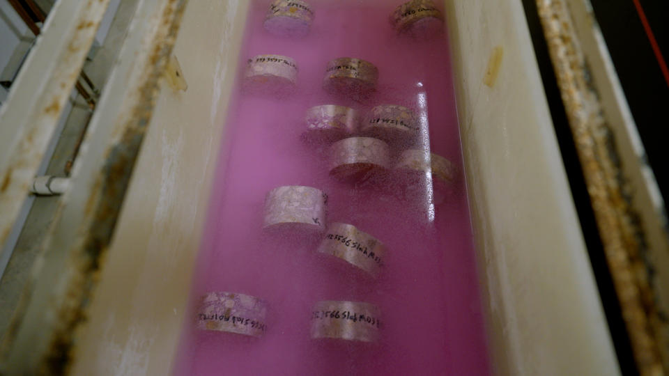 Labeled concrete samples lay in pink liquid inside a trough. 