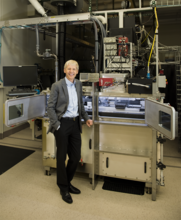 NIST Chief Metrologist Jim Olthoff stands in front of equipment in a lab. 