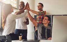 Group of coworkers in office celebrating with a high five.