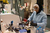 SURF student Zainab Altamimi, who wears a hijab, stands in a lab with safety glasses and gloves on as she holds a micropipette in one hand and a vial in the other.